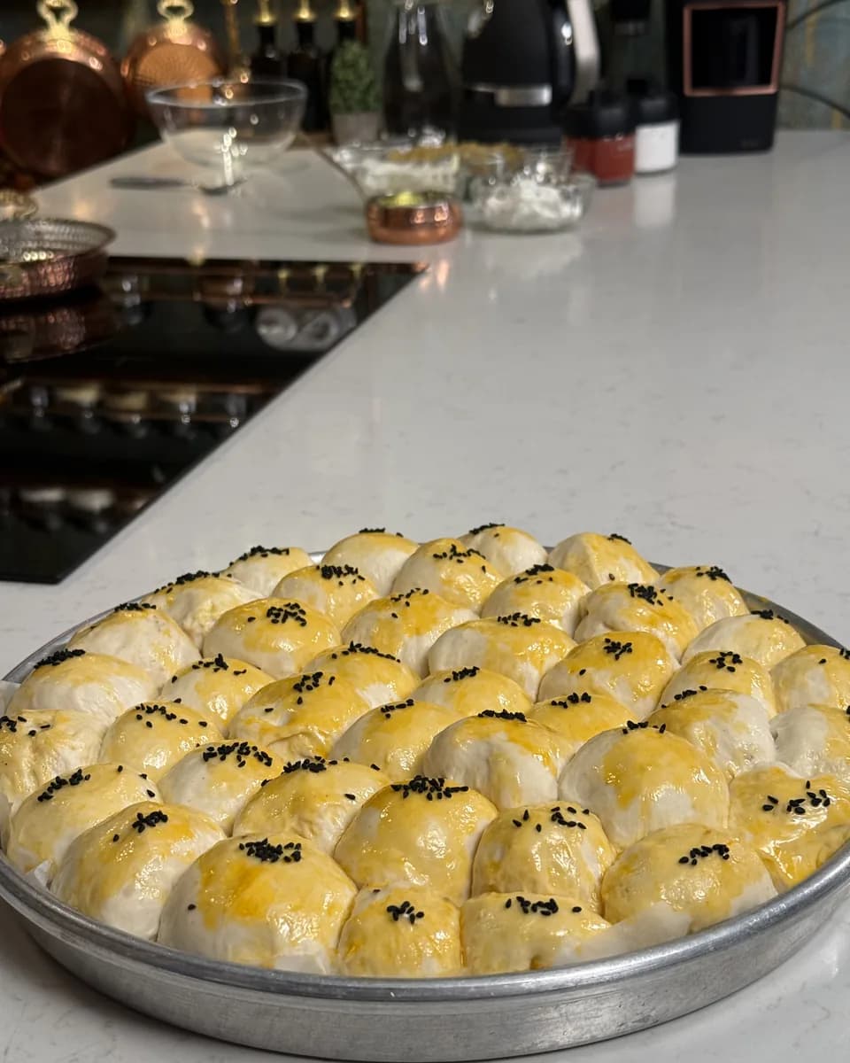 Metal yuvarlak tepside sıra sıra dizilmiş, yumurta sarısı sürülüp çörek otu serpilmiş pişmemiş hamur topları